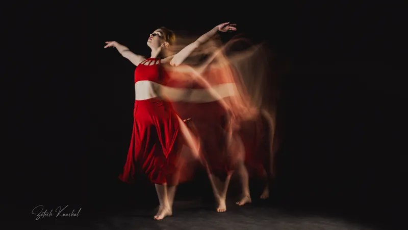 Dancer in red with arms raised, captured in a long exposure with motion trails against a dark background
