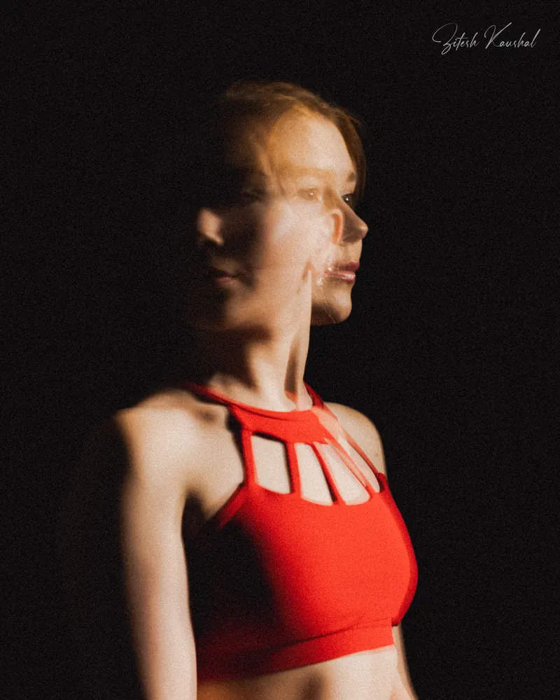 Close-up portrait of a dancer in a red cut-out top, with multiple-exposure motion blur against black