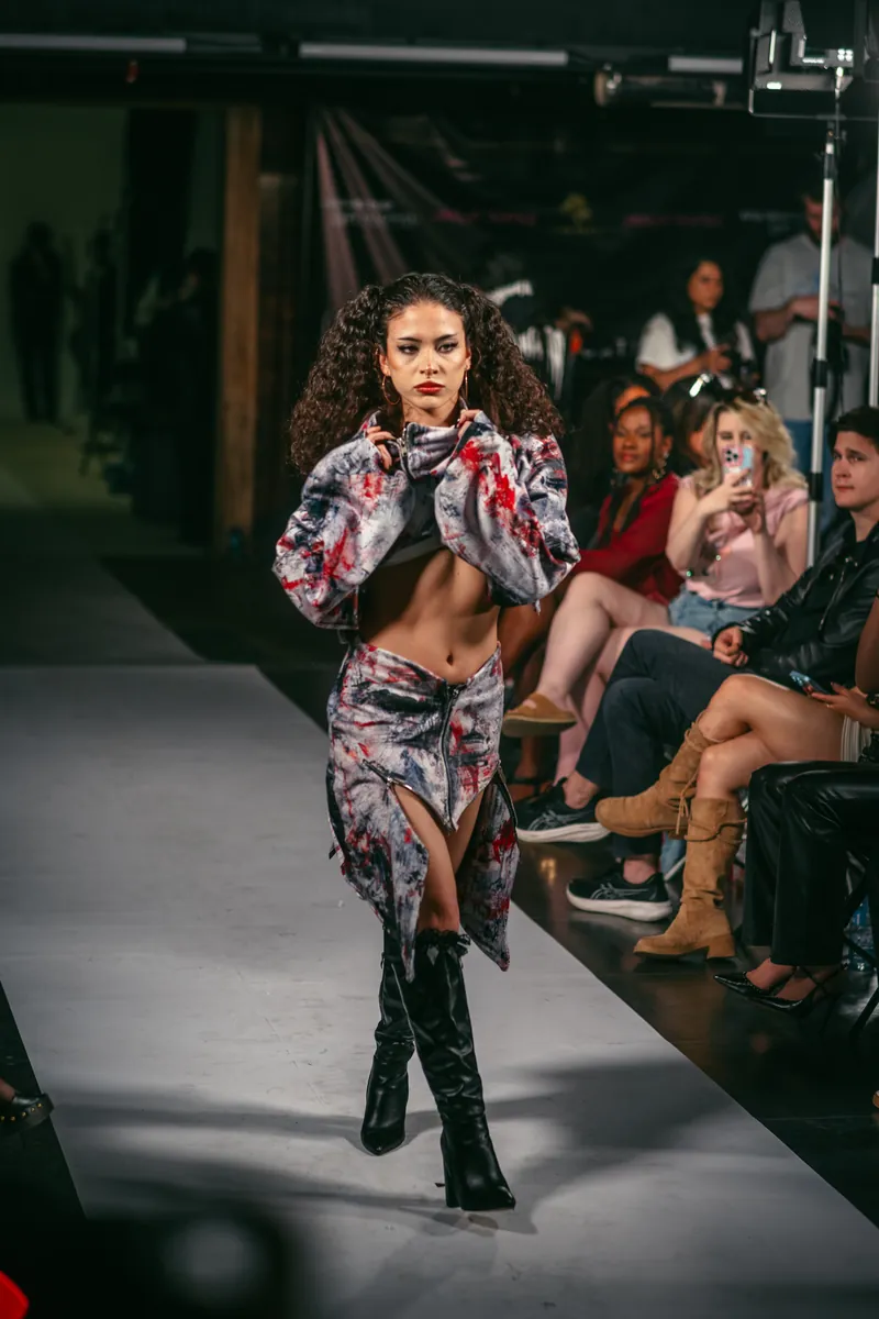 Model with curly dark hair in a patterned jacket and skirt walking the runway