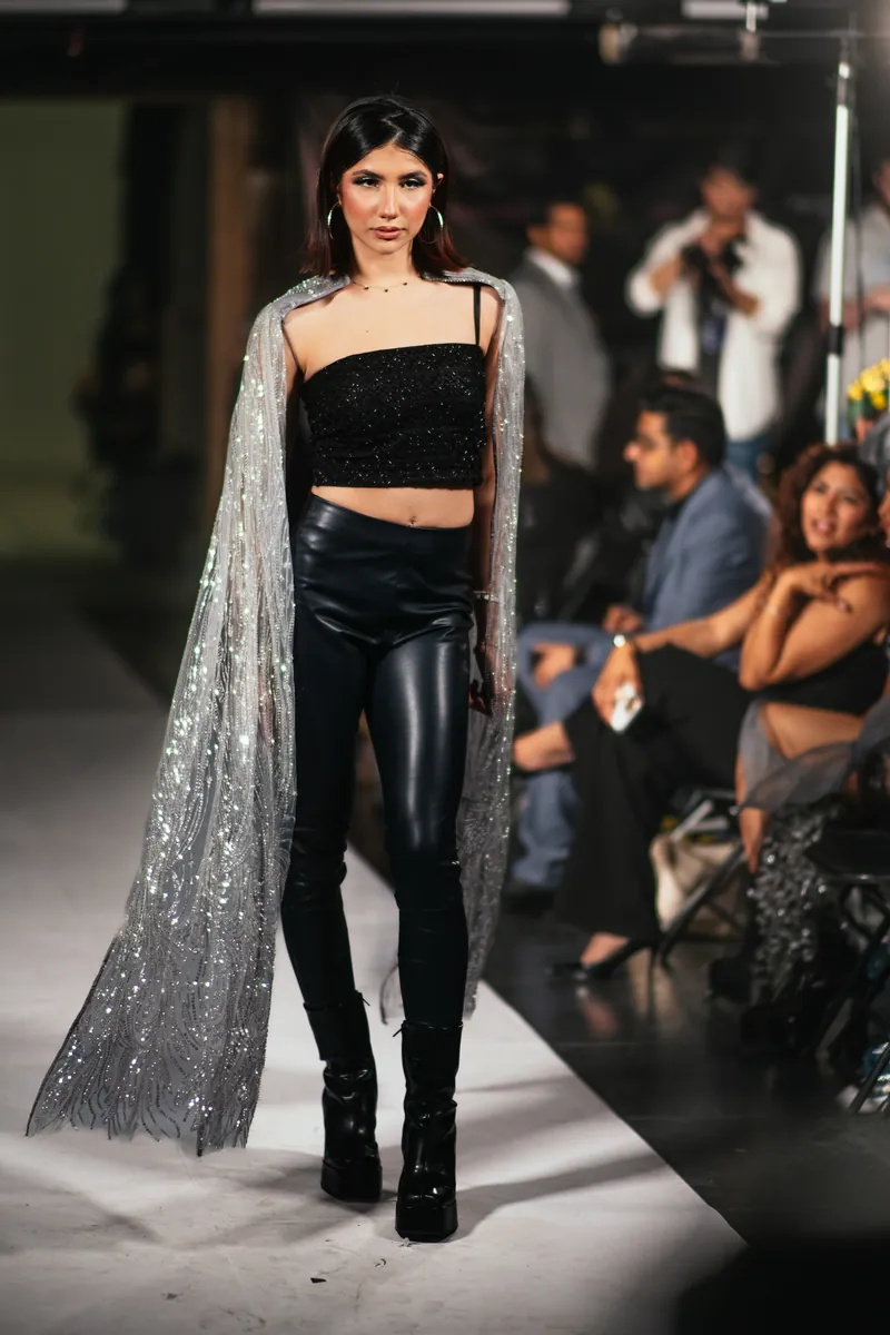 Model in a black top, leather pants and a sparkling sheer cape on the runway