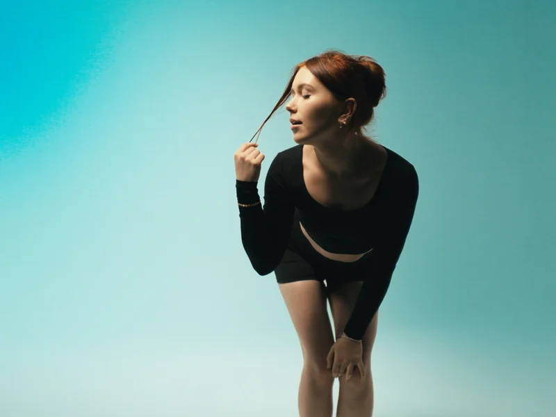 Revival still: model leaning forward looking away, REVIVE crop top and shorts, teal background