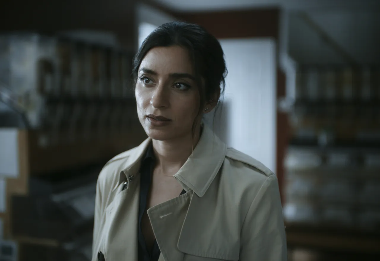 Writ Or still: close-up of a woman in a beige trench coat looking off-camera in a library