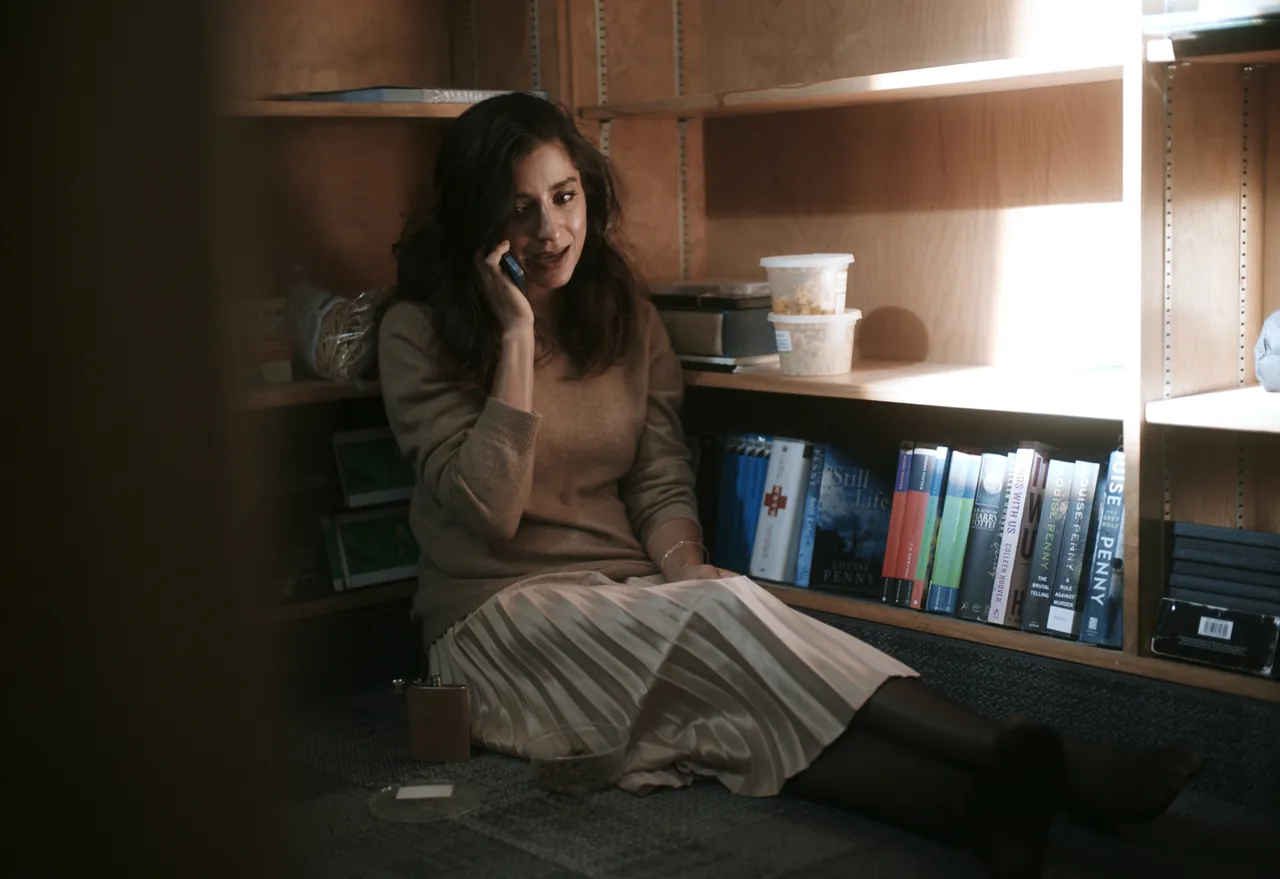 Writ Or still: a woman sitting on the floor between bookshelves, talking on a phone
